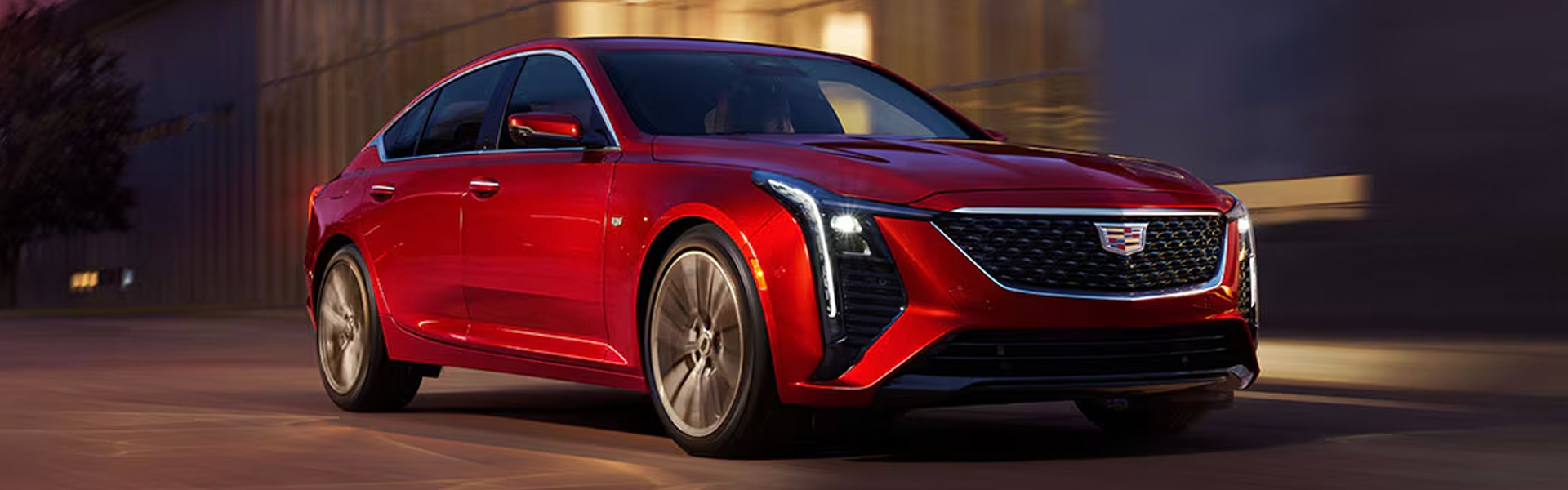 Red Cadillac CT5 luxury sedan driving on a city street.