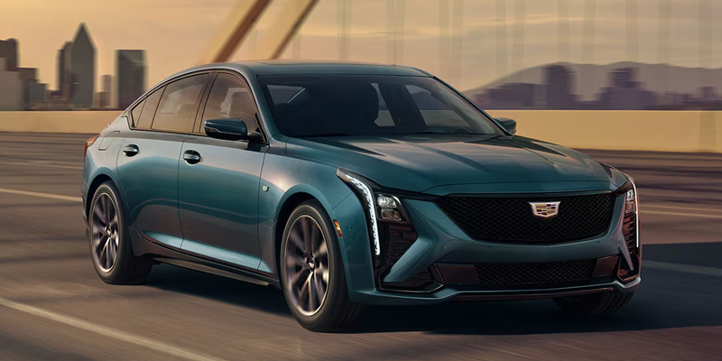 Teal Cadillac CT5 sedan driving along a city road.